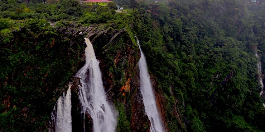 Multiple cascades of a massive waterfall plunge down a deep, lush green gorge, one of the best among Tripura waterfalls.