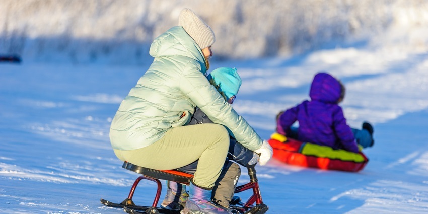 An image of a kid enjoying the sledging activity with his mother in snowy peak