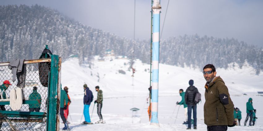 Man entering the snow covered skiing area with people standing in the background, Sikkim.