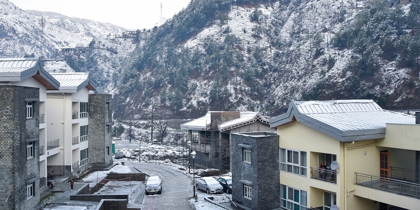 Aerial view of streets and houses of Himachal Pradesh with forested hills in the background.