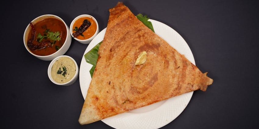 A golden-brown, crispy dosa on a white plate with sambhar and chutneys at South Coast Restaurant, one of the restaurants on GS Road Guwahati.