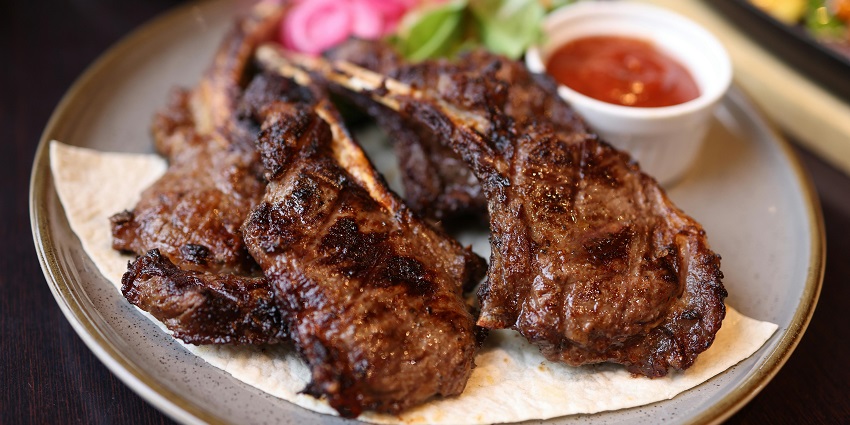 Grilled lamb chops with a side of salad and a dipping sauce served at Spring Valley Restaurant.
