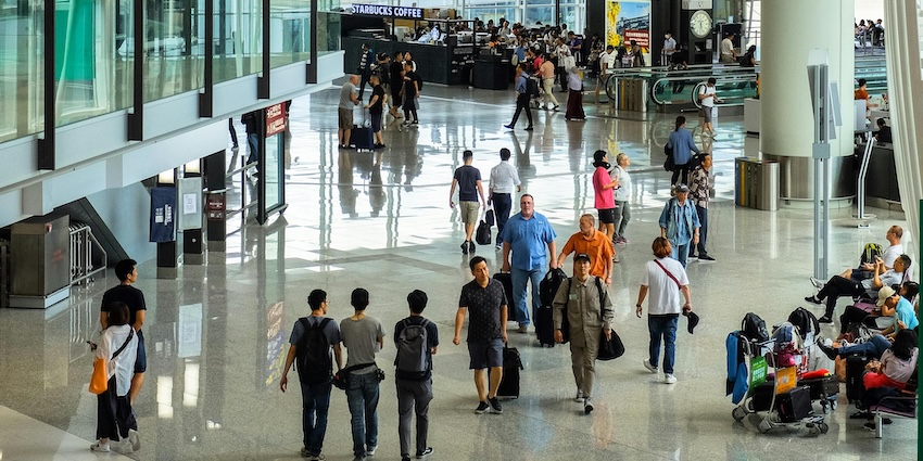 Travellers walking through a busy airport terminal with shops, seating, representing airports in Tripura.