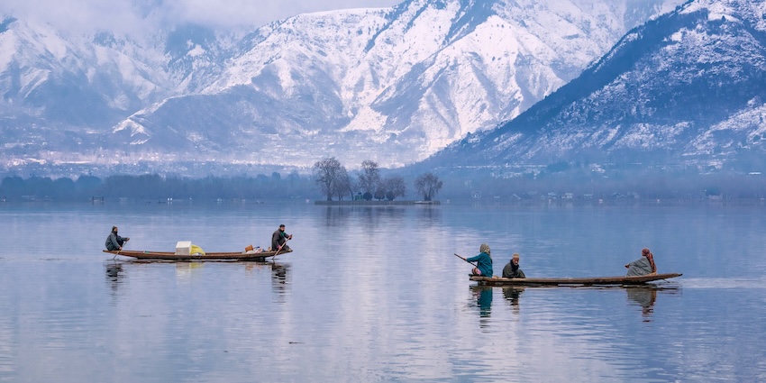People rowing boats on the icy waters of Dal Lake against the backdrop of snow mountains