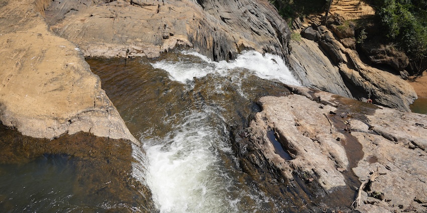 Overhead view of a river plunging over a rocky, brown cliff ledge into a dark pool.