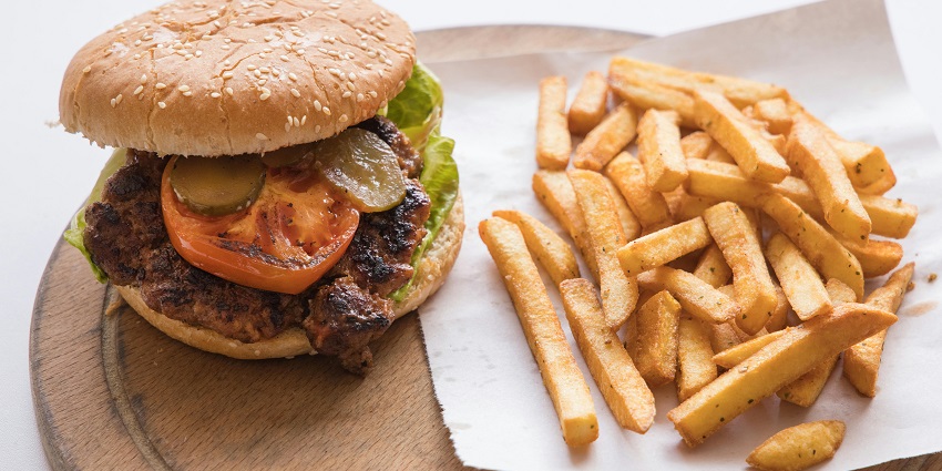 A grilled burger with tomato, pickles, and fries served on a wooden platter.