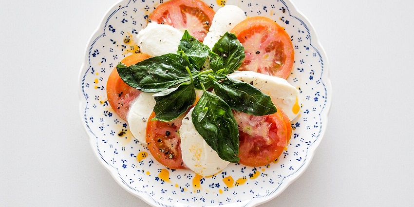 A close-up of a fresh Caprese salad with tomato, mozzarella, and basil, drizzled with oil.