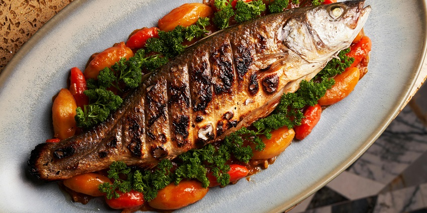 Grilled whole fish with vegetables served on a ceramic platter at a restaurant.
