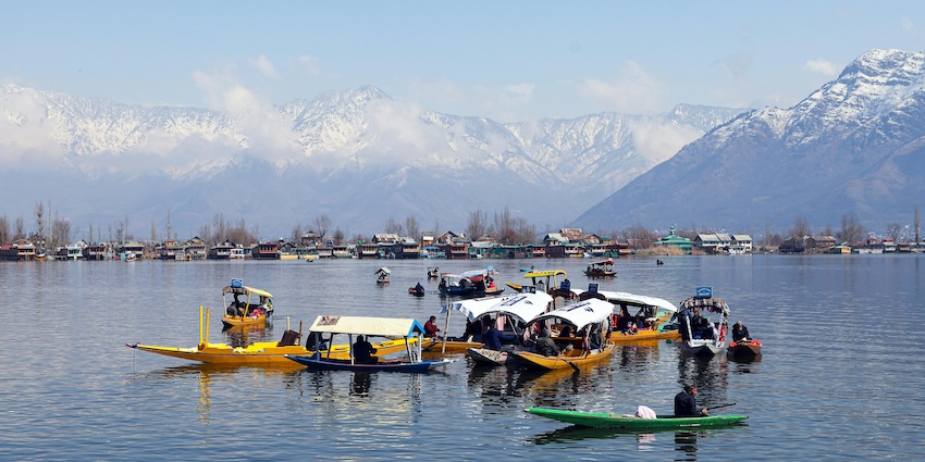 Several boats on the large water body of a lake in Srinagar and distant huge snowy mountains.