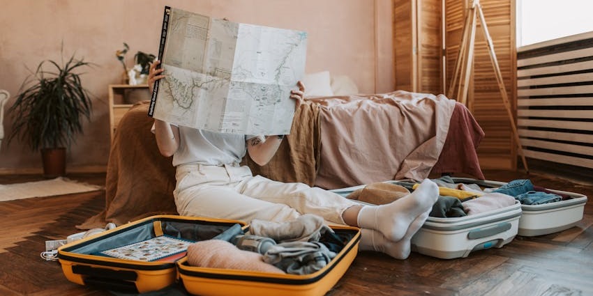A person sitting on the floor packing suitcases and reading a map while planning a trip.