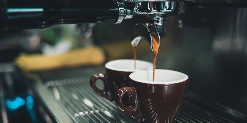 Fresh espresso pouring into two brown cups from a professional coffee machine.