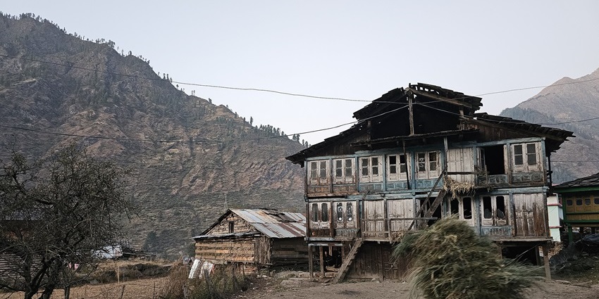 Traditional wooden house in Tosh village, Himachal Pradesh, with a local carrying a hay bundle