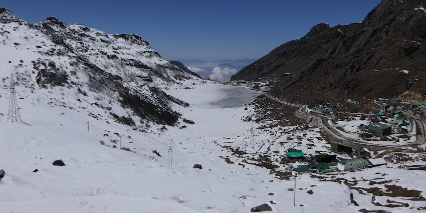 Frozen Tsomgo Lake surrounded by snow-covered mountains with snowfall in Gangtok.