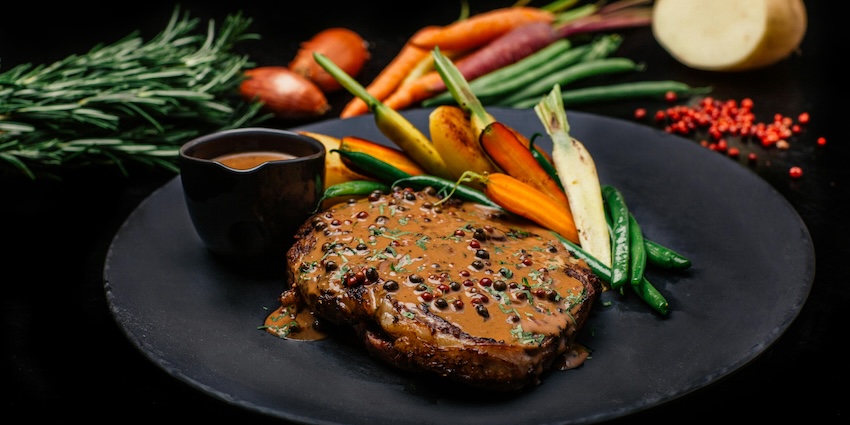Grilled steak with pepper sauce served with colourful roasted vegetables on a dark plate