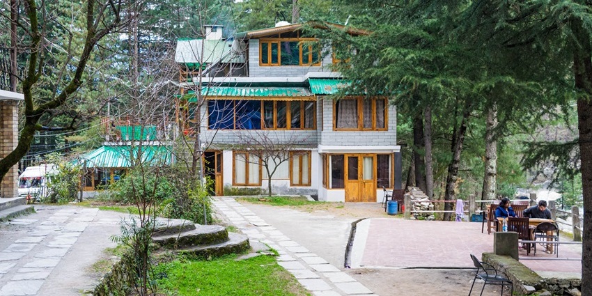Open-air restaurant at Hotel Alpine in Kasol, surrounded by pine trees and mountain views