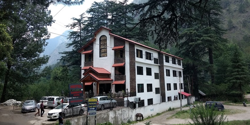 Hotel Sandhya in the Kasol valley is surrounded by tall pine trees and mountain landscape views, showing snowfall in Kasol.