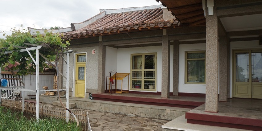 Cosy traditional homestay with tiled roof, open porch, yellow doors, and small garden.