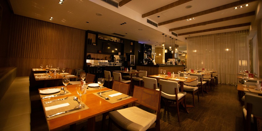 Elegant restaurant interior with wooden tables, cushioned chairs, and soft evening lighting, one of the famous restaurants in Jorhat.
